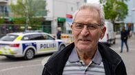 Seniorimies seisoo ulkona kesällä kadulla ja hänen takanaan näkyy poliisiauto.