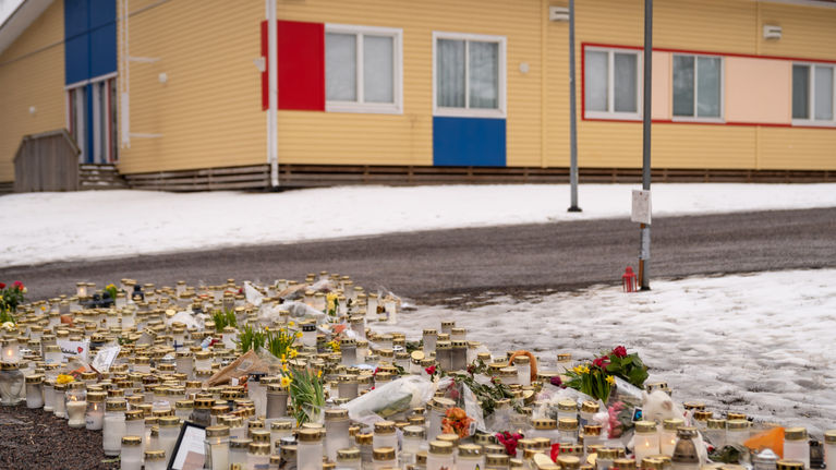 Candles, stuffed animals, flowers, and cards on the ground in front of the school.