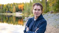 Siniasuinen nainen seisoo syksyisen lammen rannalla kädet puuhkassa ja katsoo kameraan.