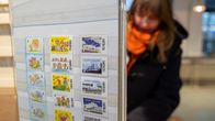 Asiakas tekemässä pakettia Postin toimipisteessä ja etualalla postimerkkejä.
