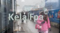 Woman wearing pink coat walking in the rain on a city sidewalk, seen through a mist-covered window embossed with the Kela/Fpa logo.