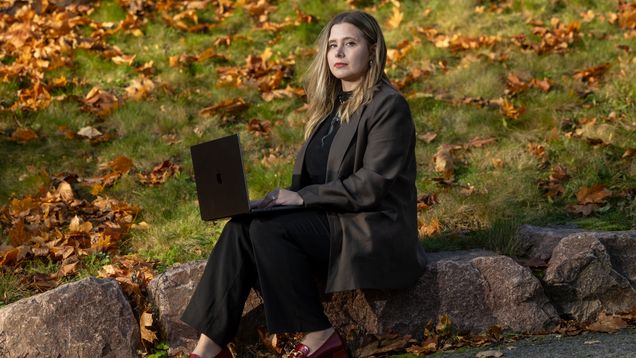 Laura Kankaala istuu läppärin kanssa kivellä syksyisessä maisemassa.