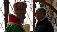Moskovan patriarkka Kirill puhuu Venäjän presidentille Vladimir Putinille ikkunan edessä. Kirill on pukeutunut kirkolliseen asuun, Putinilla on musta päällystakki.