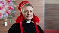 Kirkon saamelaistyön sihteeri Erva Niittyvuopio yllään musta saamenpuku, papin kaulus ja punainen saamelaisnaisen lakki.