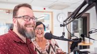 Kuvassa mies ja nainen radiostudiossa. He hymyilevät radiolähetystä tehdessään.