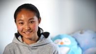 Fotbollsspelaren Queenie Xiang ler mot kameran i sitt flickrum med mjukisdjur i bakgrunden.