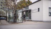 En person med cykel står vid en taxihållplats utanför en vit tegelbyggnad.