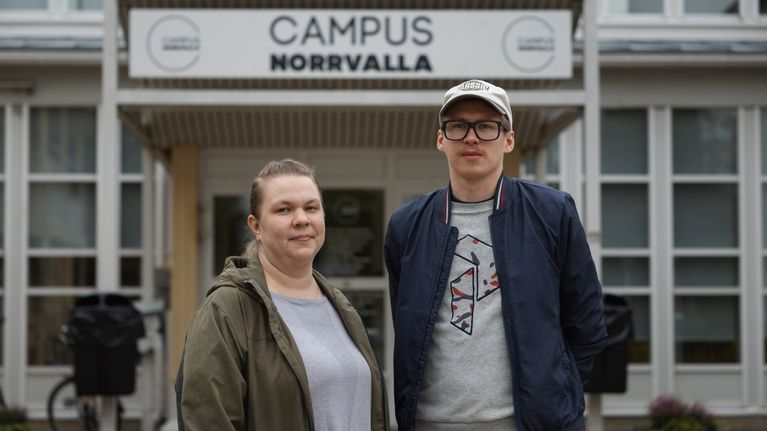 Två personer står framför entrén till en byggnad med skylten "Campus Norrvalla" ovanför dörren.