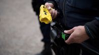 Detail of a person wearing a blue police uniform holding a yellow electric stun gun.