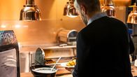 Man taking food from a restaurant buffet counter.