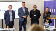 Kolme miestä ja yksi nainen rivissä Lumo kylttien edessä.