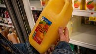 En kund i en matvaruaffär håller i en stor flaska apelsinjuice.