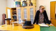 Memmu Lankila nojaamassa työpöytään. Pöydällä valmis tohtorinhattu ja monta keskeneräistä hattua.