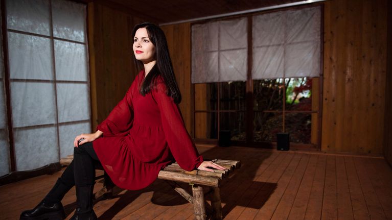 Kirjailija Elina Pitkäkangas istuu penkillä, punainen mekko päällä.