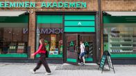 Två personer går förbi och in genom entrén till Akademiska bokhandeln, med gröna skyltfönster och texten "AKADEMINEN AKADEMEN" synlig.