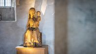 Puinen madonna-veistos kirkon seinällä, valossa kylpevässä huoneessa.