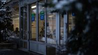 Sairaalan ulko-ovi, hattupäinen mies istuu sairaalan käytävällä.
