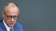 Erittäin huolestuneen näköinen, puoliksi kalju ja silmälasipäinen mies sinisessä puvuntakissa ja kravatissa tuijottaa lähikuvassa oikealle.