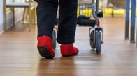 Lähikuva vanhuksesta, joka kävelee rollaattorin kanssa.