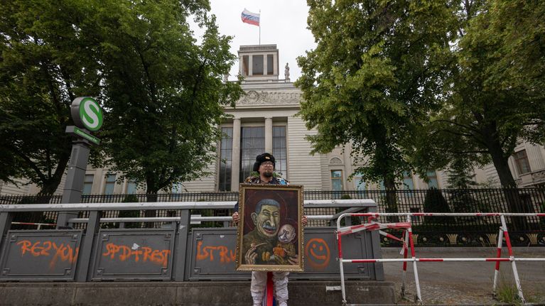 Den ryska konstnären Robert Kuzovkov, alias Semyon Skrepetsky, står framför Rysslands ambassad i berlin. I famnen håller han ett portätt av Josef Stalin som håller Rysslands president Vladimir Putin i famnen.
