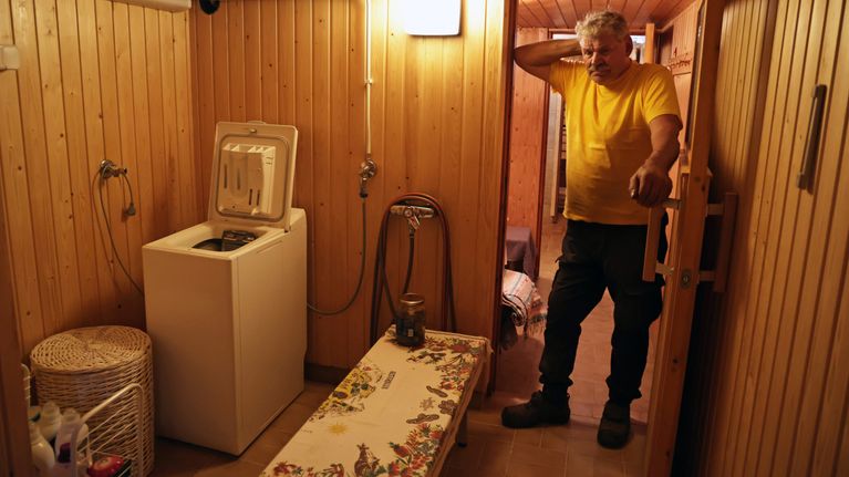 Mies seisoo mökkinsä kellarikerroksen kodinhoitohuoneessa, jossa on pyykinpesukone.