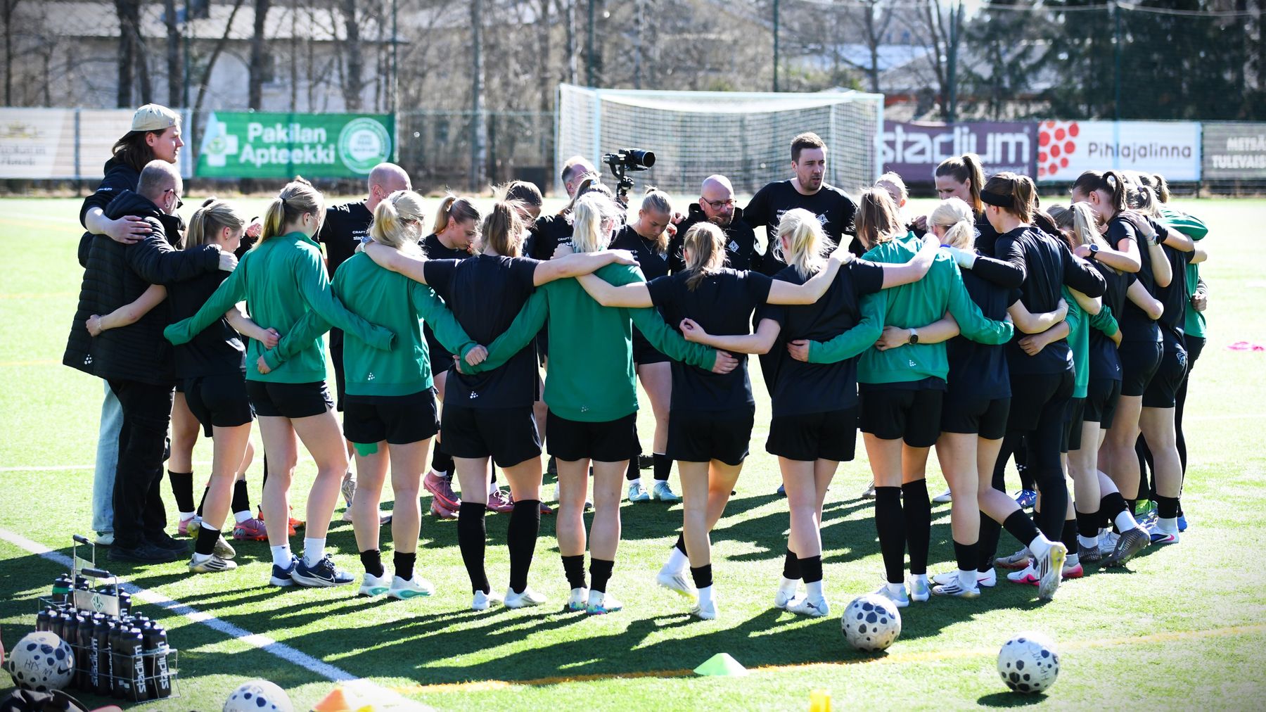 Helsingin Palloseuras damlag står i ring med armarna om varandra på en solig fotbollsplan.