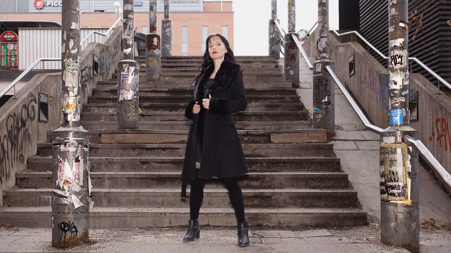Dess Terentjeva seisoo rautatieaseman alikulkuun johtavilla rappusilla takki liehuen. Laaja kuva.