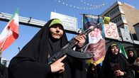 Iranilaisnainen pitelee asetta mielenosoituksessa, taustalla Ali Khamenein suuri kuva.