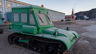 Vanha vihreä lumitelaketjullinen pieni ajoneuvo. Takana puinen punainen kirkko.