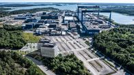 En illustrerande bild av varvet Meyer Turkus nya huvudkontor med kranar och omgivande skog vid vattnet.