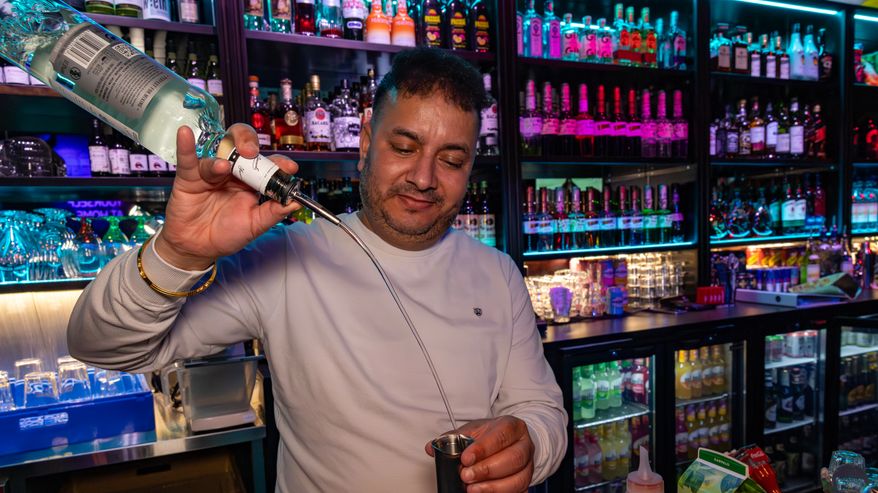 Mies seisoo baaritiskin takana ja kaataa kippoon laajalla kaarella juotavaa alkoholipullosta.