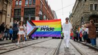 Kaksi valkopukuista henkilöä kantaa Helsinki Pride -lippua.