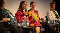 Paneelikeskustelussa saamenpukuun sonnustautunut Christina Hæatta puhuu mikrofoniin. Taustalla myös kaksi naista ja yksi mies.