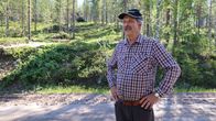 Mies musta lippalakki päässään seisoo metsän reunassa.