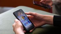 Händer håller i en mobiltelefon med en spelapp öppen.