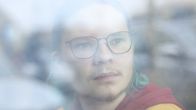 Henkilö seisoo sumuisen ikkunan takana kaupungin katumaisemassa.