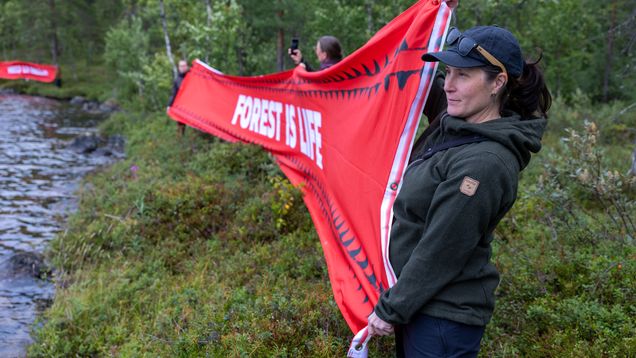 Henkilöitö pitämässä punaista banderollia järven rannalla.