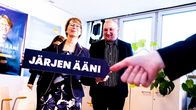 Sari Essayah järjen ääni vaalikyltti kädessään vaalivalvojaissa. Taustalla ehdokkaana ollut Kauko Pohjanen.