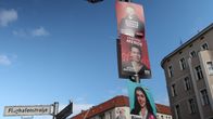 Tre valaffischer med bilder och namn på politiker sitter på en lyktstolpe vid gatuskylten "Flughafenstraße". Bilden är tagen i Neuköln i Berlin.