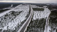Flygfoto över ett snöklätt landskap med avverkad skog och en väg som slingrar sig genom skogen och en elkraftledning som löper parallellt med vägen.