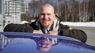 Ilkka Porttikivi nojaa autoon ja katsoo hymyillen kameraan.