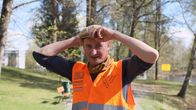 Oranssiin huomioliiviin pukeutunut kuvataiteilija Kimmo Ylönen sovittelee päähän lakkia keväisessä puistossa.