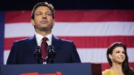 Floridas guvernör Ron DeSantis i röd slips och blå kostym bakom en talarstol fotograferad snett nerifrån. 