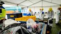 Opiskelijat lajittelevat jätteitä suojavaatteissa. Kuvassa näkyy jäteastioita ja opiskelijat lajittelemassa erilaista materiaalia teltan sisällä.