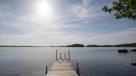 Laituri johtaa tyynelle järvelle. Aurinko paistaa kirkkaalta taivaalta.