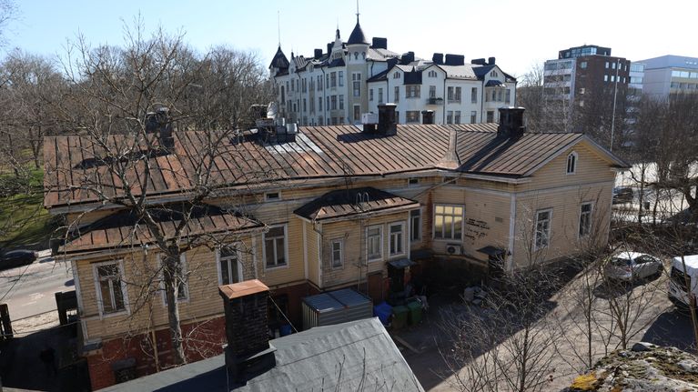 Ett gult trähus med plåttak omgivet av träd och flervåningshus i bakgrunden. I Vårdbergsparken står jugendhuset Hjorten.