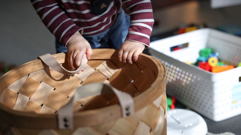 A small child's hands on a toy basket.