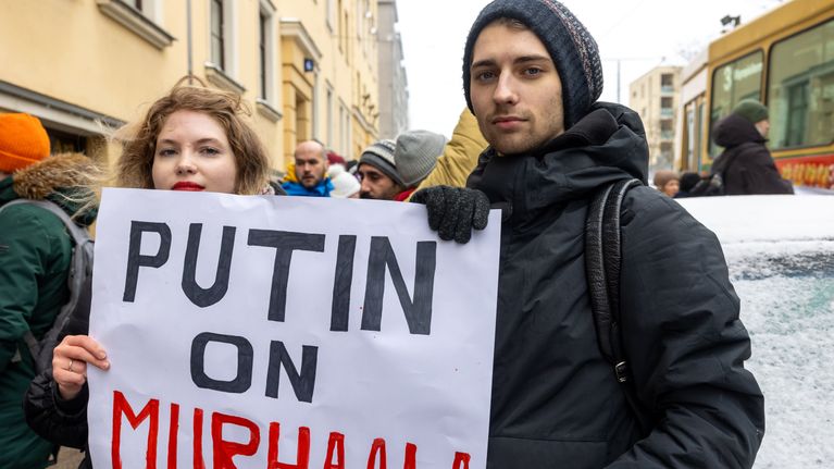 Aljena Volkova ja Andrei Volkov katsovat kameraan ja  pitelevät kylttiä, jossa lukee Putin on murhaaja.