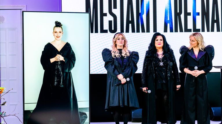 Ellinoora, Kaija Koo ja Vesala lavalla, taustakankaalla lukee Mestarit areenalla. Jenni Vartiainen on lavan vasemmalla puolella videoyhteyden kautta suurella ruudulla.