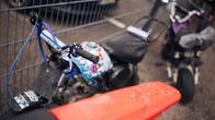 Kaksi pienikokoista motocross-pyörää pysäköitynä metalliaidan eteen märällä asfalttipinnalla. Etualalla näkyy kirkkaan punainen etulokasuoja.